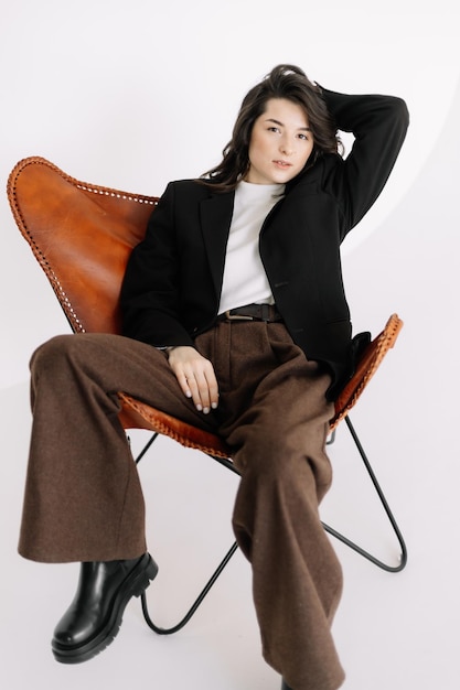 Stijlvol modieus portret van een meisje zittend op een stoel in een fotostudio op een witte achtergrond