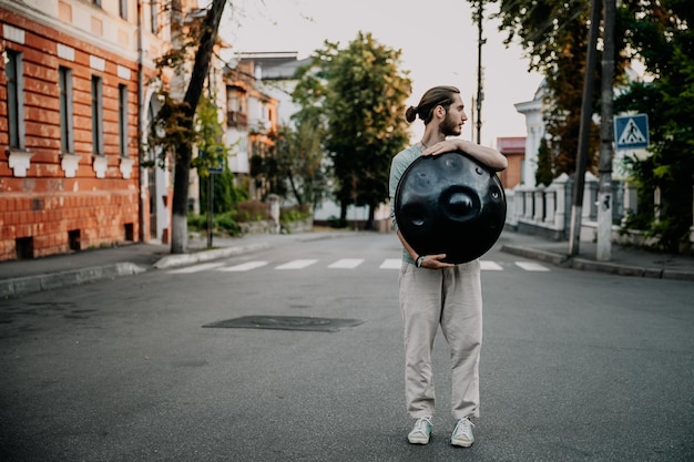 Stijlvol portret van een jonge, bebaarde hipster met een modern handpan-muziekinstrument op een stadsachtergrond