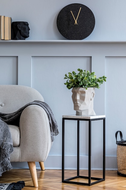 Stijlvol Scandinavisch interieur van woonkamer met grijze bank, plaid, zwarte klok, houten lambrisering met plank, marmeren kruk, planten en elegante persoonlijke accessoires in design home decor.