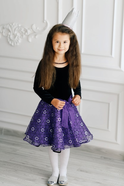 Stijlvol schattig meisje met witte speelgoedkroon in zwarte blouse en paarse rok
