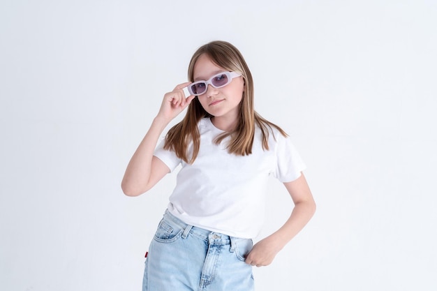 Stijlvol tienermeisje in een witte t-shirt en spijkerbroek heeft een stijlvolle zonnebril in haar handen