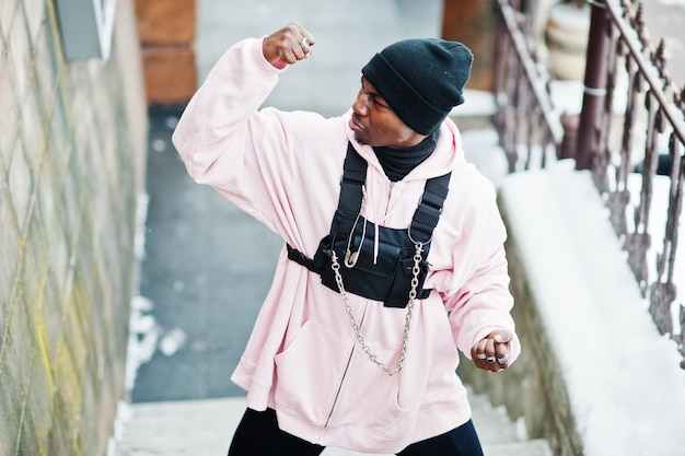 Stijlvolle Afro-Amerikaanse man in stedelijke stijl in roze hoodie geposeerd op winterdag toont de spieren op de handen