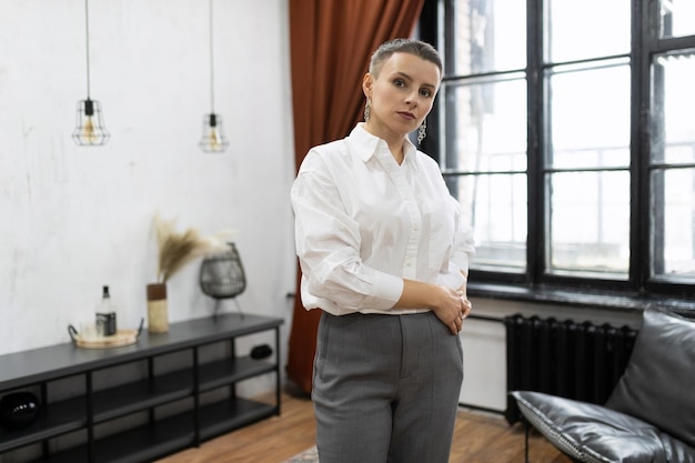 Stijlvolle authentieke blanke vrouw met een kort kapsel in een wit overhemd staat tegen de