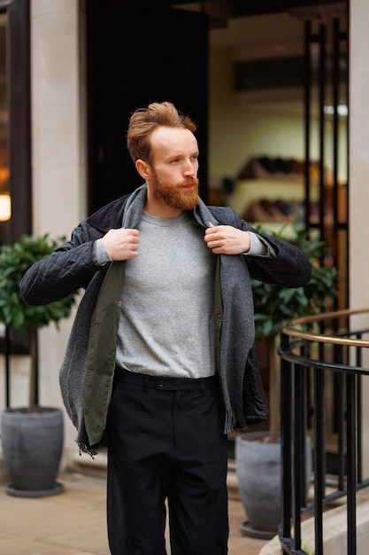 Stijlvolle bebaarde man in een jas en sjaal gaat de winkel of het restaurant uit naar de straat