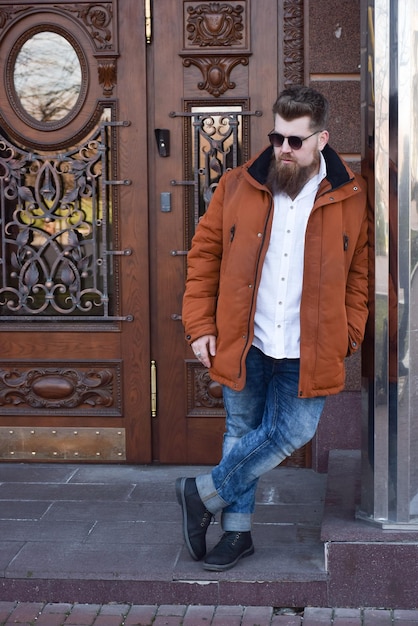 Stijlvolle blanke man in zonnebril met een lange baard op de achtergrond van decoratieve houten deuren