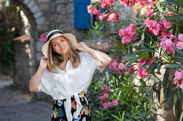 Stijlvolle blanke vrouw in stro zomerhoed en zonnebril genietend van vakantie in de oude stad met pootstenen en oude huizen Zomervakantie