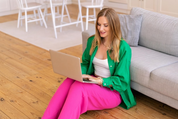 Stijlvolle blonde freelancer blonde vrouw werkt op haar laptop bij woonkamer thuiskantoor concept