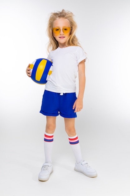 Stijlvolle blonde meisje in korte broek, een t-shirt en gymschoenen met een bril houdt een basketbal bal op een wit