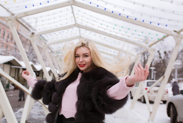 Stijlvolle blonde vrouw met lang haar in beweging poseren op straat met sneeuw