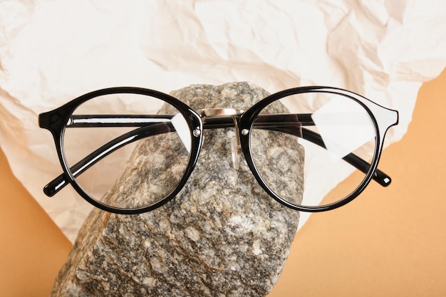 Foto stijlvolle bril op een steen op een achtergrond van verfrommeld wit papier, trendy stilleven, accessoires voor oogcorrectie close-up