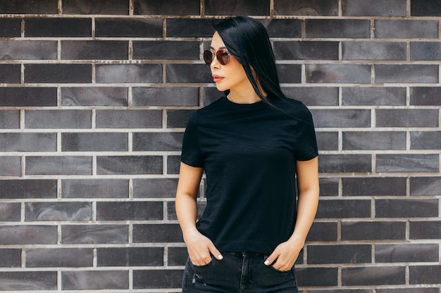 Foto stijlvolle brunette aziatisch meisje met zwarte t-shirt en zonnebril poseren tegen straat stedelijke doek