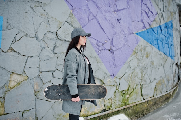 Stijlvolle brunette meisje in grijze capwith skate board