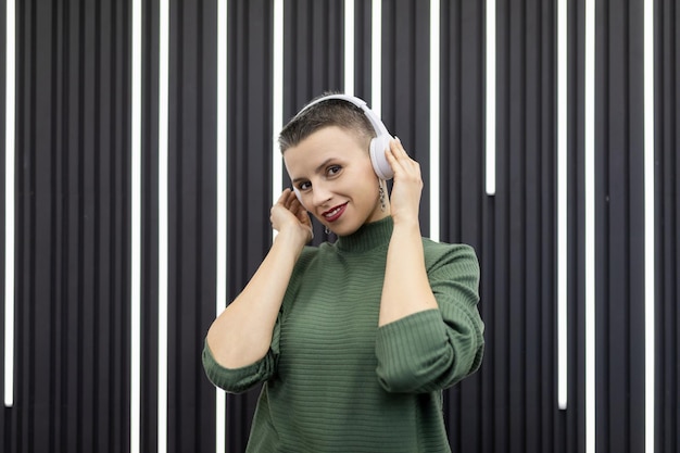 Stijlvolle caucasiaanse vrouw met kort kapsel luistert naar muziek in een koptelefoon op de achtergrond van een