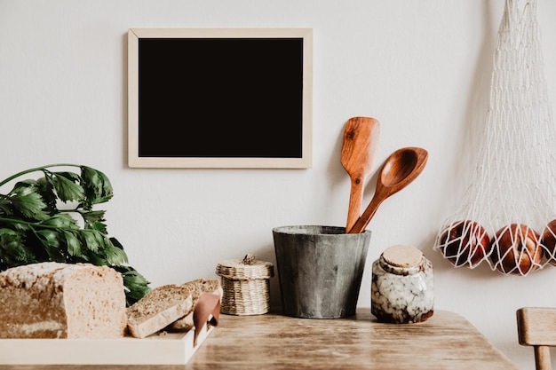 Stijlvolle compositie van creatief eetkamerinterieur met mock-up posterframe, houten tafel en stoel, bakplaten en andere keukenaccessoires Neutrale muren