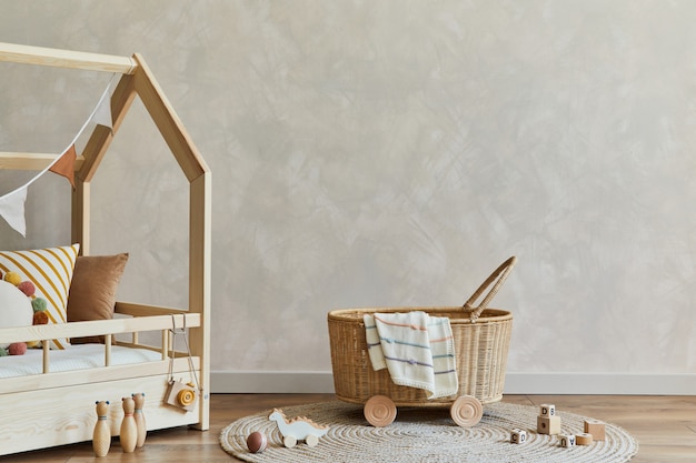 Stijlvolle compositie van gezellig scandinavisch kinderkamerinterieur met bed, rotanmand, pluche en houten speelgoed en hangende decoraties van textiel. Creatieve muur, tapijt op de vloer. Ruimte kopiëren. Sjabloon.