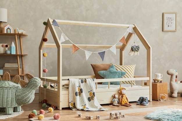 Stijlvolle compositie van gezellig Scandinavisch kinderkamerinterieur met houten bed, plank, pluche en houten speelgoed en hangende textieldecoraties. Neutrale creatieve muur, tapijt op de vloer. Sjabloon.