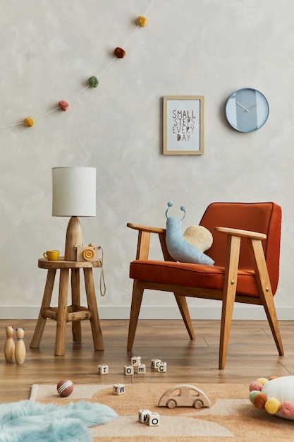 Stijlvolle compositie van gezellig scandinavisch kinderkamerinterieur met mock-up posterframe, rode fauteuil, elegante lamp, pluchen speelgoed en hangende decoraties. Creatieve muur, tapijt op de vloer. Sjabloon.