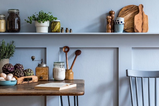 Stijlvolle compositie van keukeninterieur met houten familietafel, stoelen, groenten, kruiden, planten, fruit, voedselvoorraden en keukenaccessoires in grijs concept van woondecoratie.