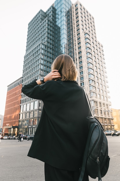 Stijlvolle dame in donkere kleding staat tegen moderne architectuur