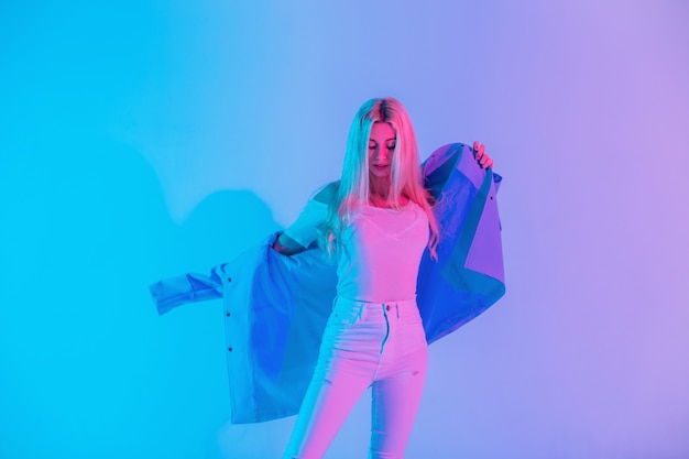 Stijlvolle elegante jonge vrouw in mode witte denim kleding kleedt blauwe blazer in studio op gekleurde neon roze lichte achtergrond. Creatieve kleurrijke vrouwelijke stijl look