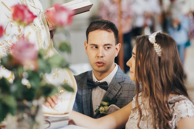 Stijlvolle emotionele bruid en bruidegom die eden afleggen en handen vasthouden aan de heilige bijbel tijdens het huwelijk