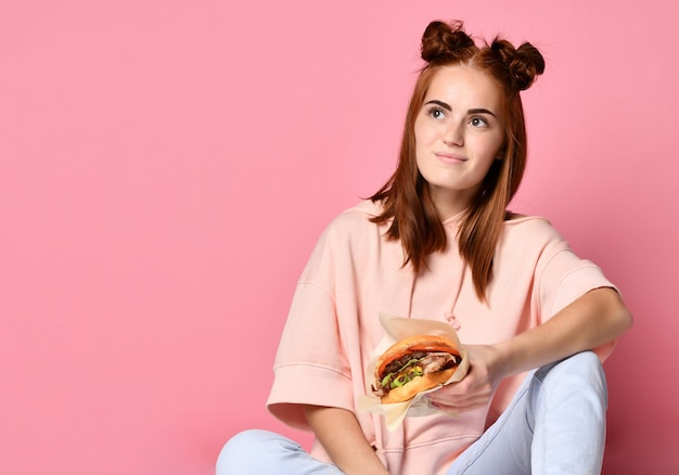 Stijlvolle en jonge gember Vrouw houdt hamburgersandwich op roze achtergrond