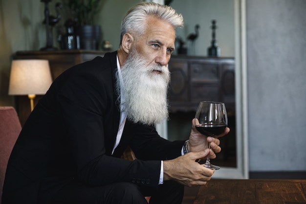 Stijlvolle en knappe bebaarde senior man rode wijn drinken