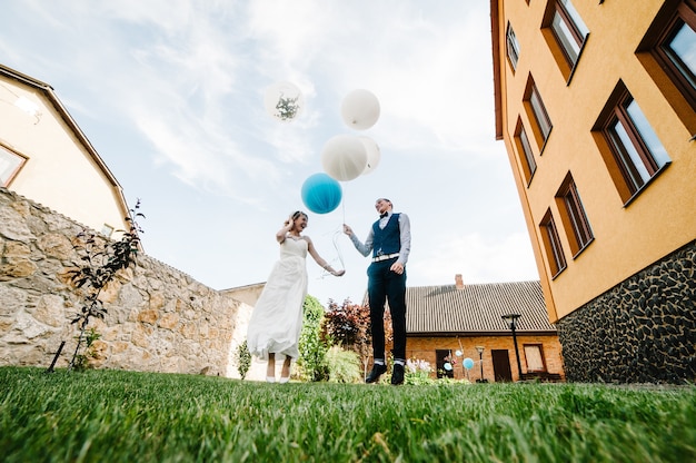 Stijlvolle gelukkige bruid en bruidegom houden ballonnen in handen en springen, poses