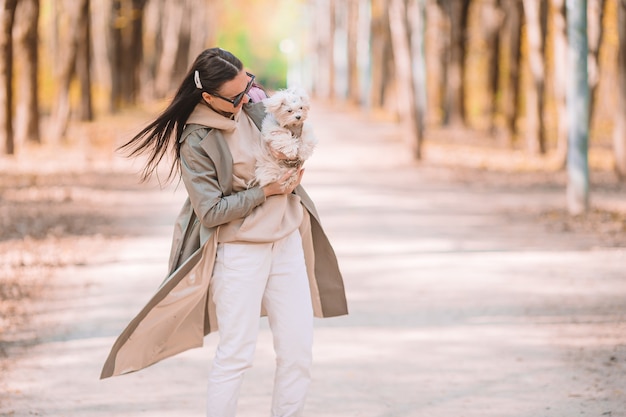 Stijlvolle gelukkige jonge vrouw, gekleed in spijkerbroek, witte sneakers wandelen met witte puppy