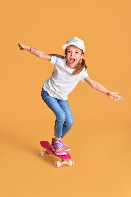 Stijlvolle grappig meisje permanent op skateboard op gele achtergrond