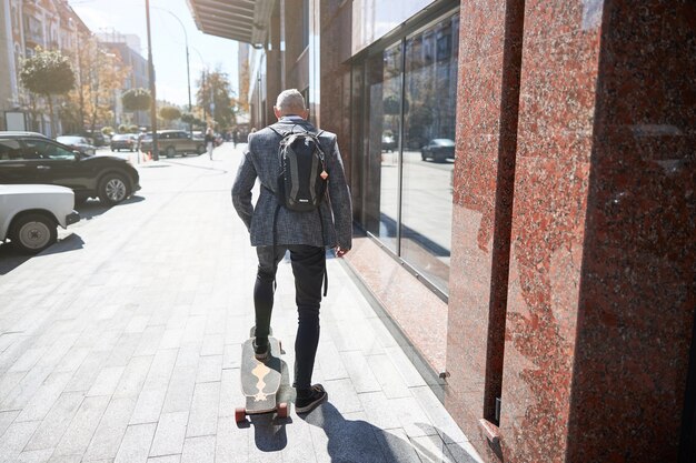 stijlvolle grijsharige man die één voet op een longboard zet