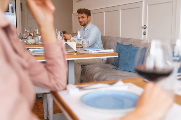 Stijlvolle heer die naar jonge vrouw kijkt en glimlacht terwijl hij aan tafel zit in restaurant