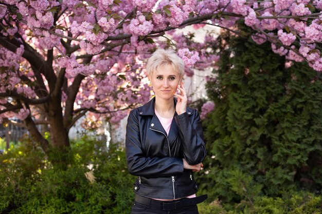 Stijlvolle hipster vrouw in de buurt van roze sakura bloeiende boom