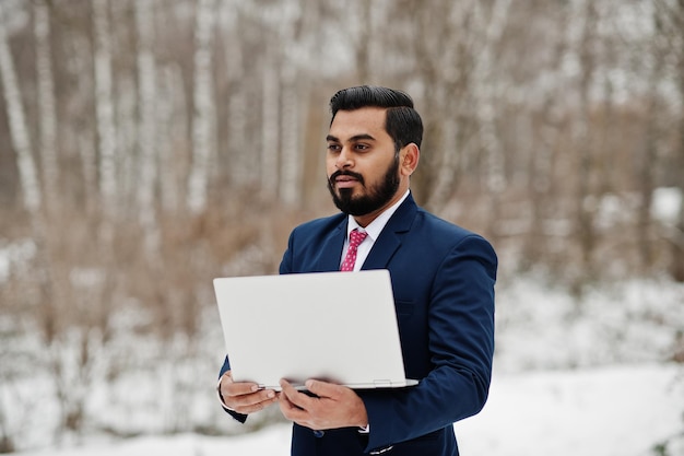 Stijlvolle indiase baard zakenman in pak geposeerd op winterdag buiten met laptop bij de hand