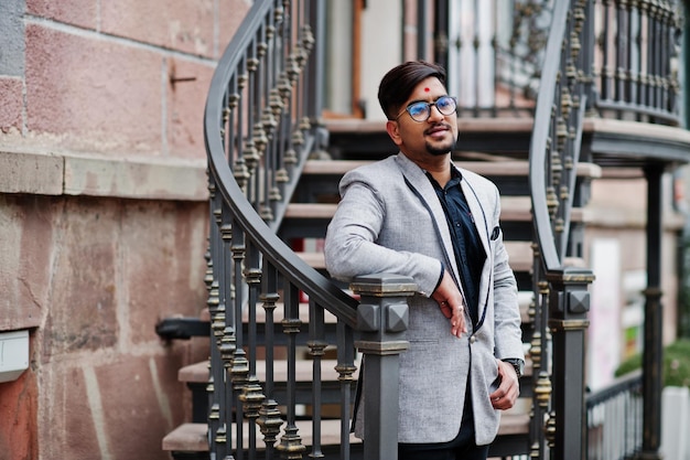 Stijlvolle Indiase man met bindi op voorhoofd en bril draagt een pak buiten tegen ijzeren trappen