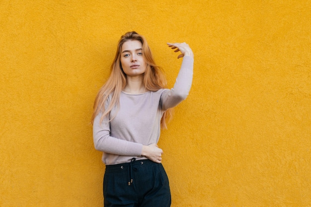 Stijlvolle jonge blonde model meisje in modieuze kleding poseren tegen een gele muur achtergrond