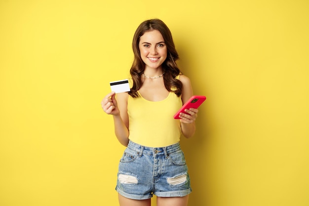 Stijlvolle jonge brunette vrouw met creditcard en smartphone betalende aankoop of iets bestellen i...