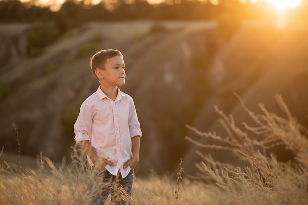Stijlvolle jonge jongen die zich voordeed op veld bij zonsondergang