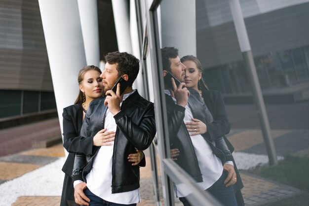 Stijlvolle jonge jongen en meisje in zwarte kleding. Een man praat aan de telefoon, een meisje omhelst een man. Houd van relaties op het werk