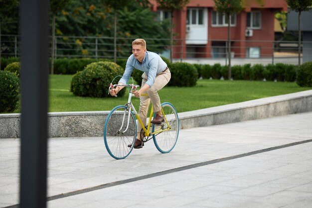 Stijlvolle jonge man kantoormedewerker werknemer rijden naar het werk op de fiets langs de straat op warme zomerdag