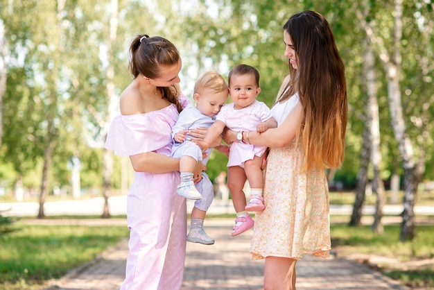 Stijlvolle jonge moeders wandelen in het stadspark met hun dochters. Mooie babymeisjes spelen met elkaar.