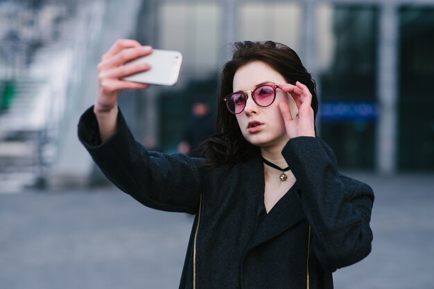 Stijlvolle jonge vrouw die selfie op de straten van de stad