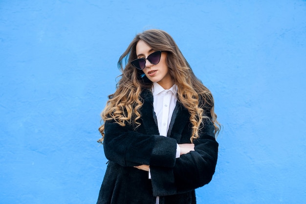 Stijlvolle jonge vrouw in bontjas op blauwe muur. Schoonheid en mode.