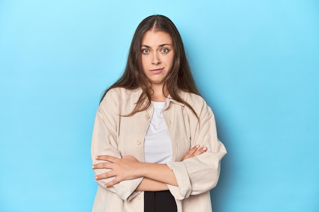 Stijlvolle jonge vrouw in een overhemd op een blauwe achtergrond ongelukkige sarcastische uitdrukking