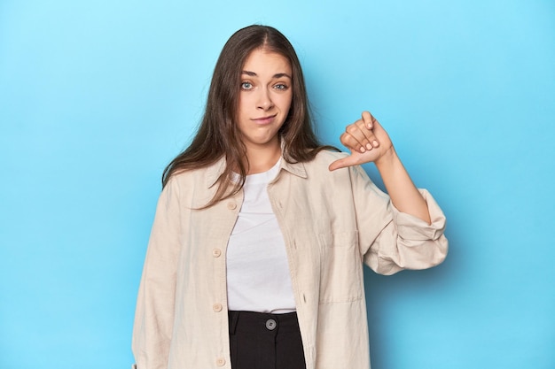Stijlvolle jonge vrouw in een overshirt op een blauwe achtergrond met duim omlaag teleurstelling concept