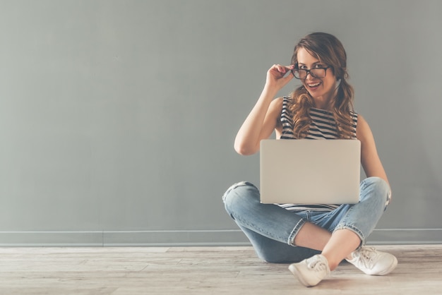 Stijlvolle jonge vrouw in glazen gebruikt een laptop.