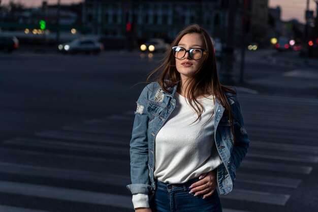 Stijlvolle jonge vrouw in glazen op straat zomertijd in de stad Portret van brunette meisje in jeugdkleren op avond stad