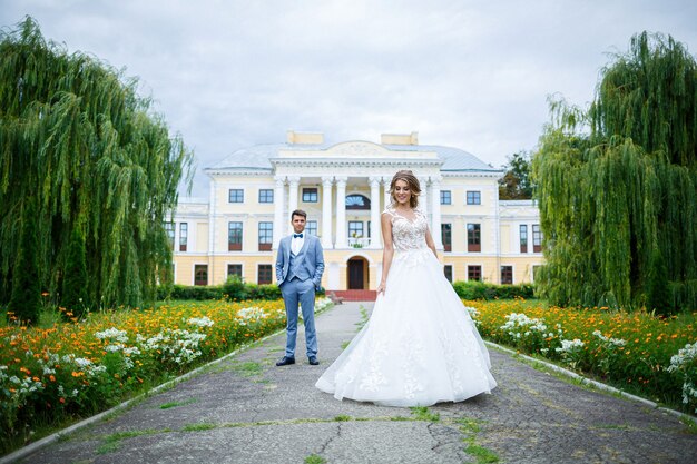 Stijlvolle jongeman in het kostuum van de bruidegom en de bruid mooi meisje in een witte jurk met een treinwandeling in het park op hun trouwdag