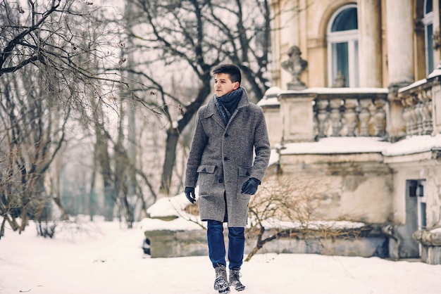 Stijlvolle jongeman in warme grijze jas en lederen handschoenen lopen in de besneeuwde straat