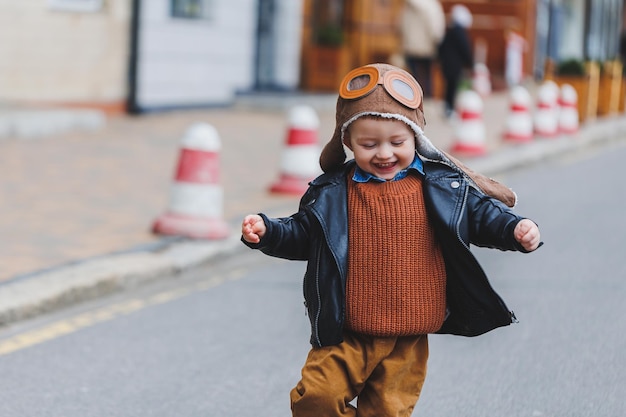 Stijlvolle jongen van 3 jaar oud in een leren jas en bruine broek loopt op straat Modern kind Kindermode Gelukkig kind